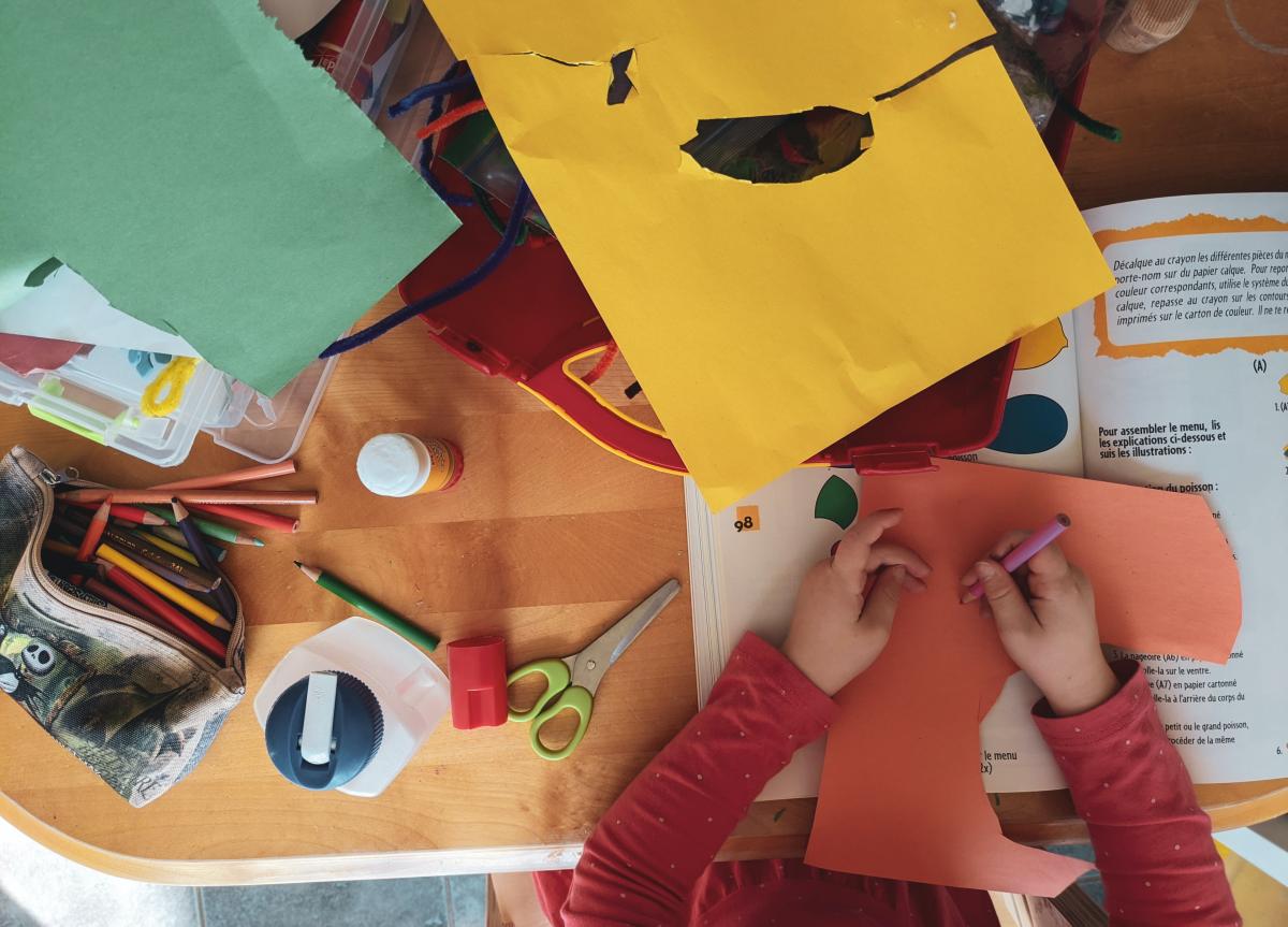 Overhead view of child cutting out and coloring construction paper