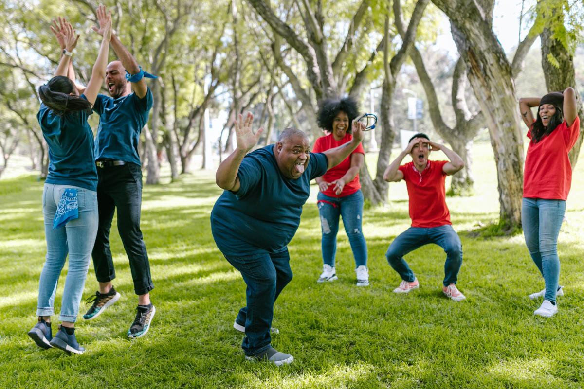 Two teams of people wearing red and blue t-shirts playing games on lawn